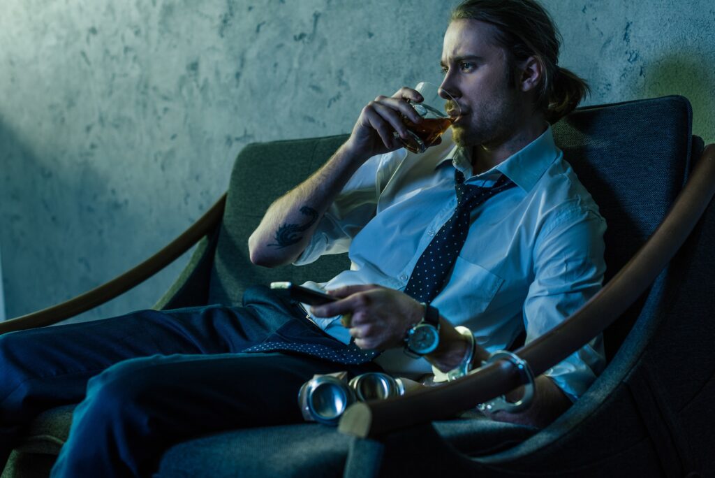 alcohol addicted man in white shirt watching tv and drinking whiskey after work